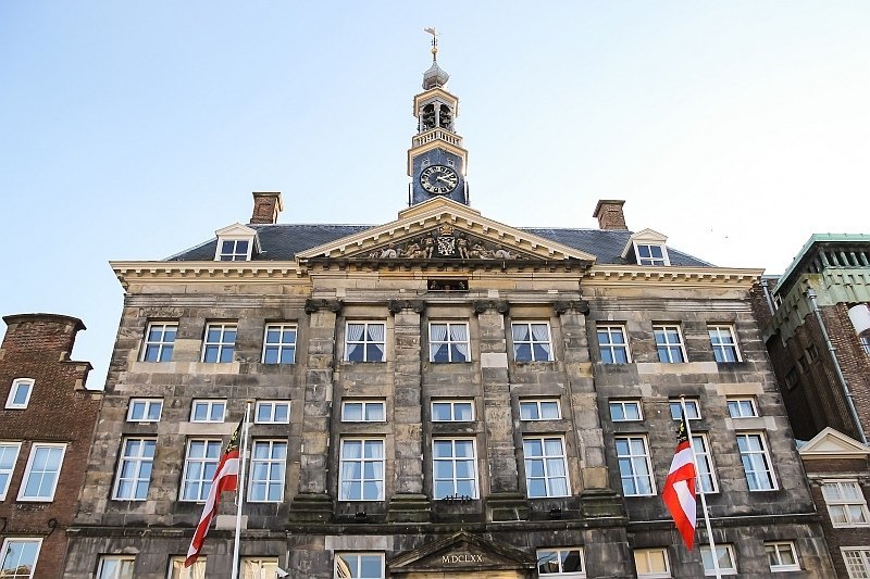 a stately building with a clock tower and two white-red flags in front, the Old Town Hall in Den Bosch