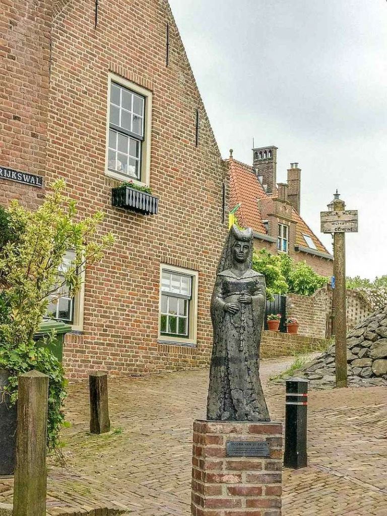 a monument of a woman in medieval clothes in front of a red-brick house, Woudrichem in the Netherlands