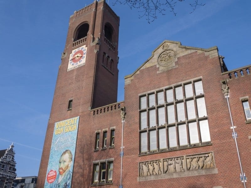 a red brick building with a clock tower and a large poster of Van Gogh on the side