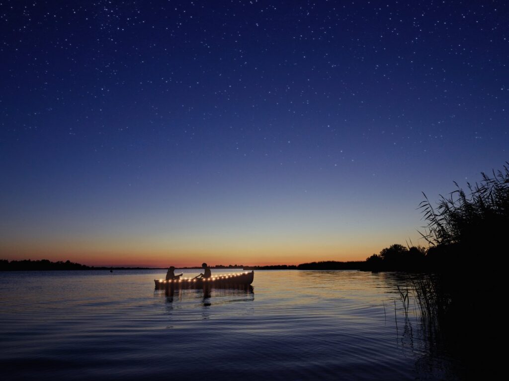 dark sky with lots of stars above a lake with a boat and two people inside, Dark Sky Park in Groningen