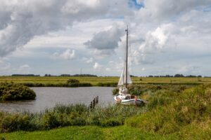 a sailing boat against a shore covered with green grass, and a cloudy sky, Lauwersmeer National Park