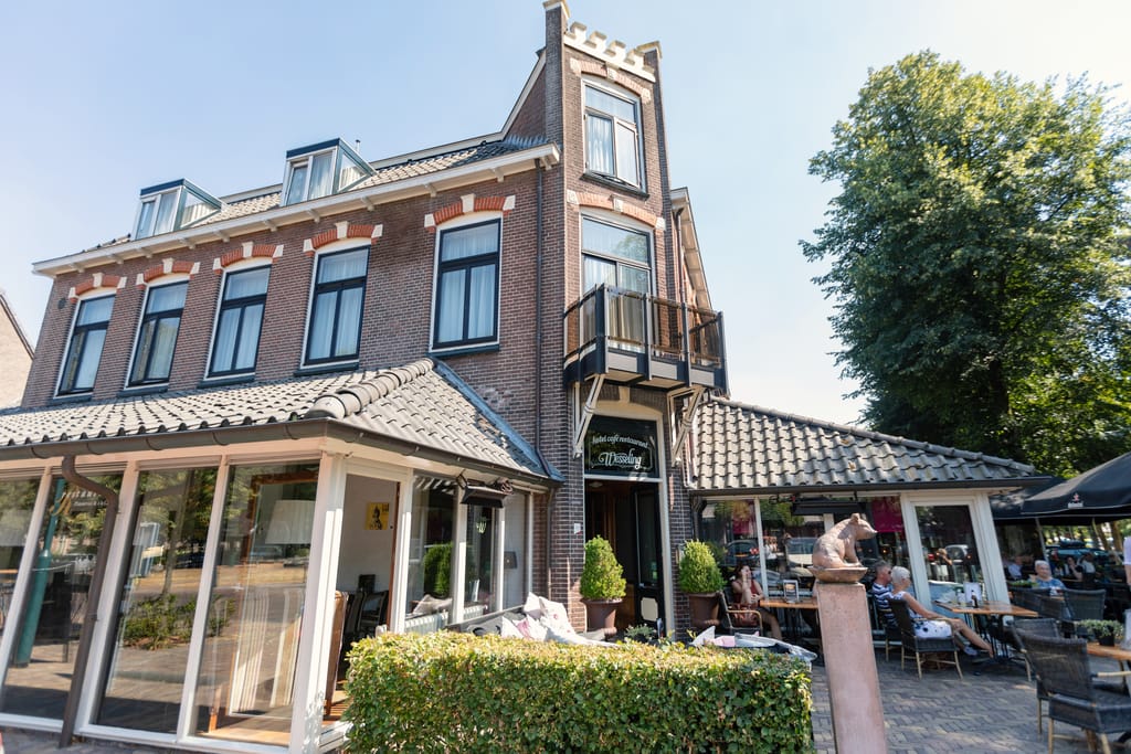 a hotel with a cafe and some tables outside and people sitting and enjoying the sunshine; Hotel Wesseling in Dwingeloo