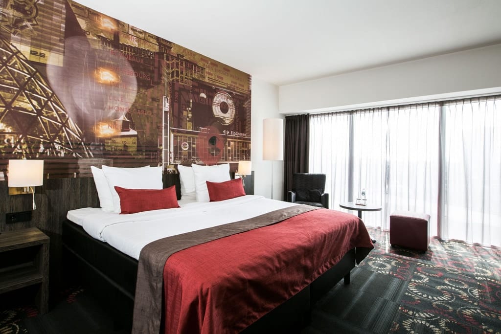A cozy hotel room at Crown Hotel Eindhoven in Eindhoven, featuring a comfortable bed, a desk, a chair, and a large wallpaper on the wall