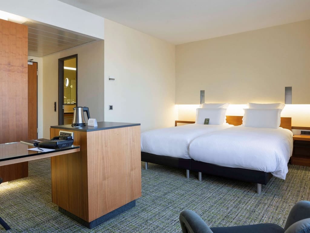 Well-appointed hotel room at Pullman Hotel Eindhoven with two beds and a desk
