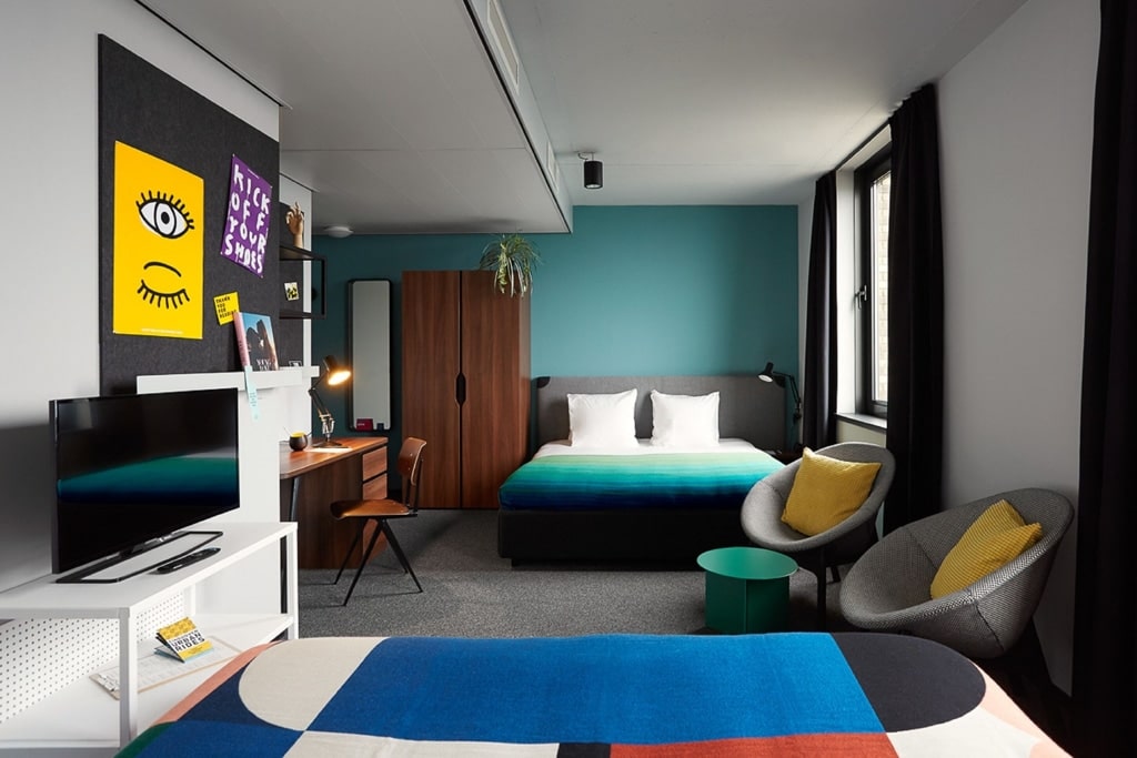 A comfortable hotel room at The Social Hub Eindhoven, featuring colorful bedding and a lively wall and carpet decor.