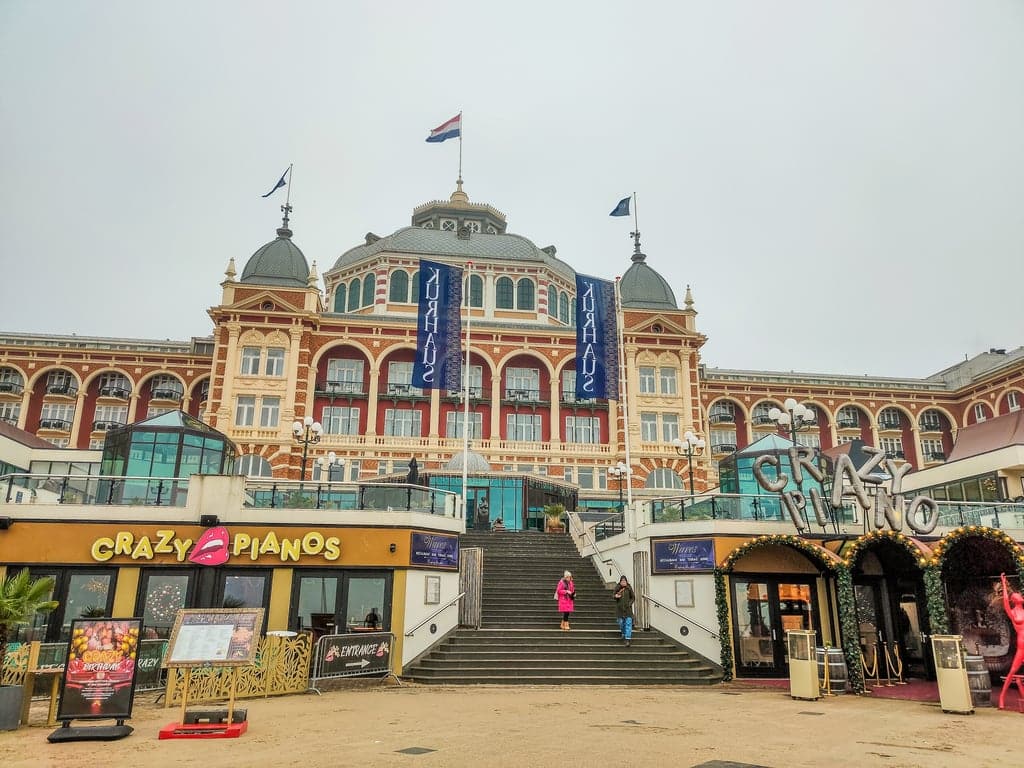 a large beautiful building with the Dutch flags on it and a staircase leading to it; Kurhaus in Scheveningen