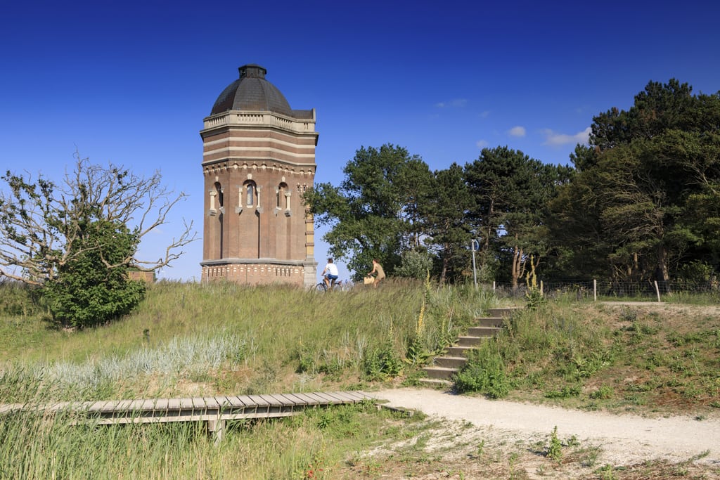 a water tower in on dune and some trees, 2 bikers cycling in front; The Water Tower at Oostduinpark in Scheveningen