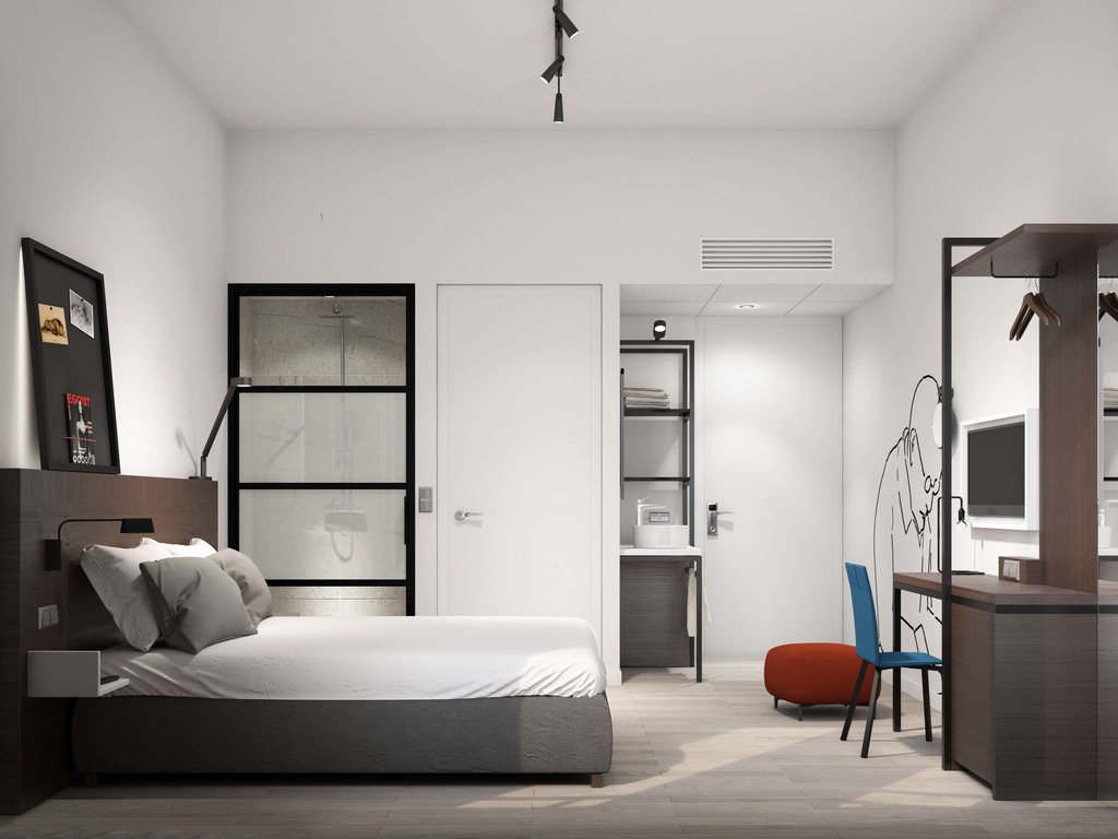 A modern, minimalist bedroom with a clean and organized design. The room features a bed with white bedding and two gray pillows, positioned against a dark wooden headboard. To the left of the bed, there is a framed picture on the wall and a wall-mounted reading lamp. Behind the bed, there is a glass door leading to a shower area. On the right side of the room, there is a desk with a blue chair and a red ottoman. Above the desk, there is a wall-mounted television. There is also a coat rack with hangers and a shelf above it. A room at the ibis Styles Den Haag City Centre Hotel
