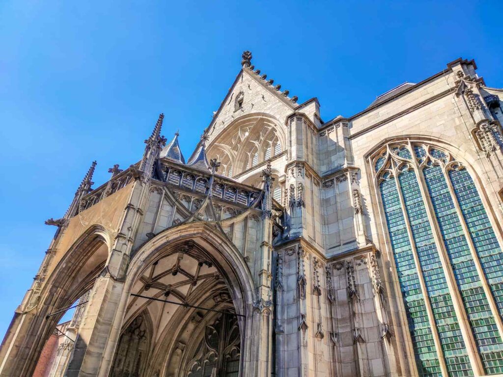 A low-angle view of a Gothic-style cathedral with pointed arches, ornate stonework, and tall stained glass windows against a bright blue sky. Stevenskerk in Nijmegen